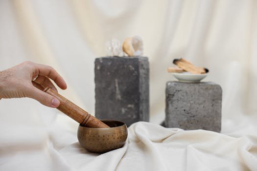 Serene setup with singing bowl, Palo Santo, crystal, and hand for meditation or relaxation ambiance.